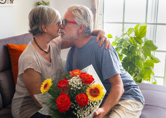 Nice elderly couple at home. They embrace and kiss to celebrate Valentine's Day with a large bouquet of flowers