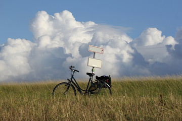 Fototapeta premium a bicycle against a sign post at the sea dyke along the westerschelde and big white clouds in a blue sky