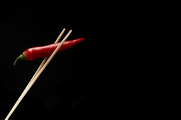 hot red pepper hold chopsticks on a black background