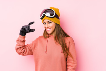 Young caucasian woman wearing a ski clothes isolated holding something little with forefingers, smiling and confident.
