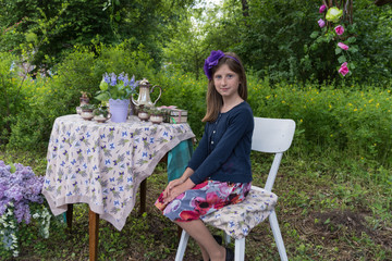 Portrait of a beautiful little girl sitting at a table in a flowered garden