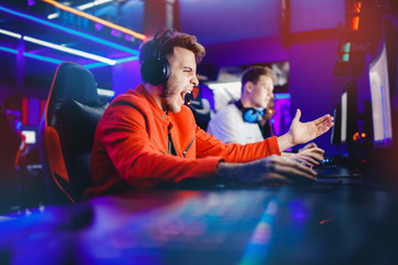 Streamer young man rejoices in victory professional gamer playing online games computer with headphones, neon color © Parilov