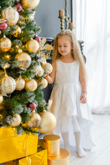 Little blonde girl in a beautiful white dress decorates a Christmas tree.