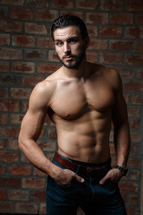 Fototapeta na wymiar Young attractive athletic guy with a naked torso on a background of a brick wall.