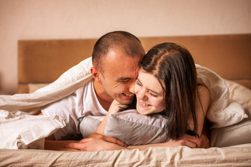 Happy couple lie on a bed covered with a blanket over their head.