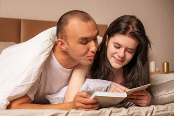 Valentine  happy couple lie on the bed and read a book