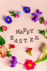 Happy Easter letters with different spring flowers around them, flat lay, pink background