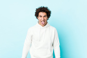 Young sporty man against a blue background funny and friendly sticking out tongue.