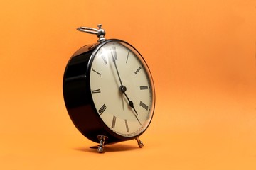 A portrait of a small old fashioned antique alarm clock with roman numbers on the dial on an orange...