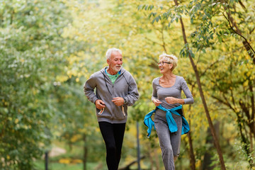 Cheerful active senior couple jogging in the park. Exercise together to stop aging.
