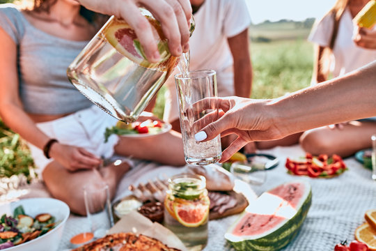 Male hands pouring lemonade from the decanter into a glass tumbler, glass pitcher with slices of grapefruit, lime, water, mint leaves - Powered by Adobe