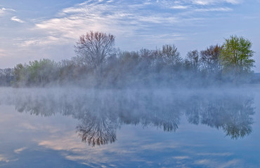 Spring landscape at sunrise of Jackson Hole Lake in fog with reflections in calm water, Fort Custer State Park, Michigan, USA