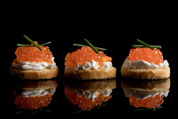 Caviar, three snacks of red caviar on bread isolated on black background with reflections, copy space