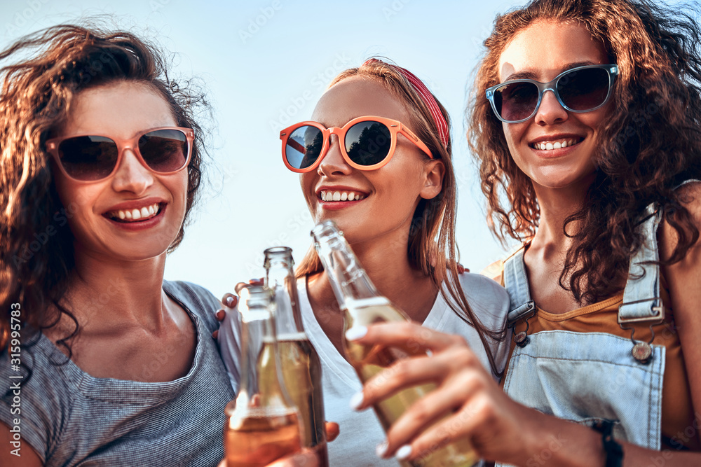 Wall mural three young women standing and clinking beer together.