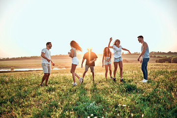 Six friends dancing, cheering on a green meadow near lake, being happy about vacation.