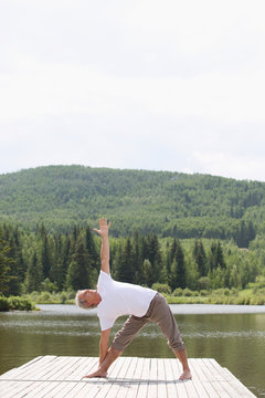 senior man doing yoga pose at the end of boat dock