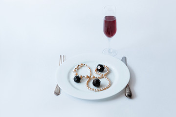 Obraz na płótnie Canvas White plate with necklace and black crystals on it, fork, knife and glass of champagne on a white background