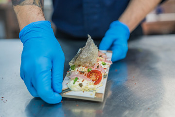 Chef hands with blue gloves presenting a plate of modern food with sea salad and cod crust tomato and spices