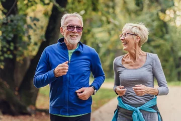 Zelfklevend Fotobehang Cheerful active senior couple jogging in the park. Exercise together to stop aging. © lordn