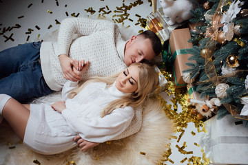  Couple lying on floor near Christmas tree and gifts. Young couple staying at home together on holiday evening. Cute romantic lovers. Couple lying on floor near Christmas tree and gifts. 
