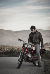 Fototapeta na wymiar motard homem sentado na moto vermelha antiga nas montanhas