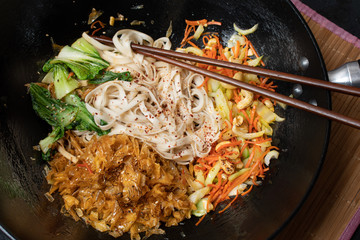 Vegan stir fry consisting of yuba, carrot, bok choy and noodles, served in wok