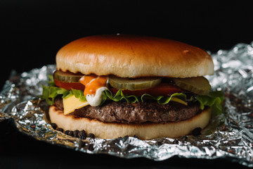 Big sandwich - hamburger burger with beef, pickles, tomato and tartar sauce on black background.