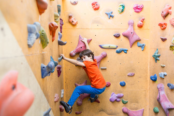 Obraz na płótnie Canvas Boy climbing on artificial boulders wall in gym