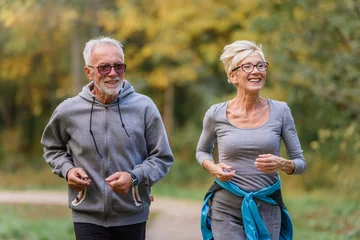 Tuinposter Cheerful active senior couple jogging in the park. Exercise together to stop aging. © lordn