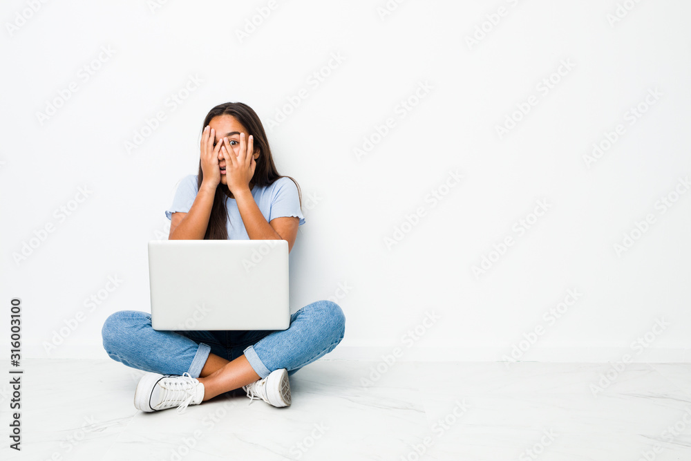 Wall mural young mixed race indian woman sitting working on laptop blink through fingers frightened and nervous