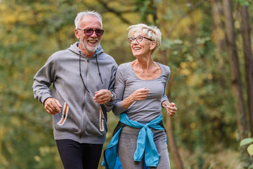 Cheerful active senior couple jogging in the park. Exercise together to stop aging.