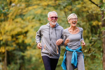 Cheerful active senior couple jogging in the park. Exercise together to stop aging.