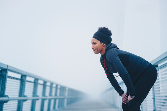 A woman resting on a bridge during exercising on a foggy day.
