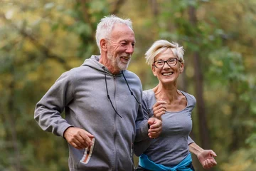 Fotobehang Cheerful active senior couple jogging in the park. Exercise together to stop aging. © lordn