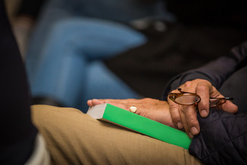 Man sitting with book on his lap and reading glasses in his hand at book launch.