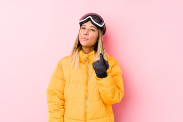 Young caucasian woman wearing a ski clothes in a pink background pointing with finger at you as if inviting come closer.