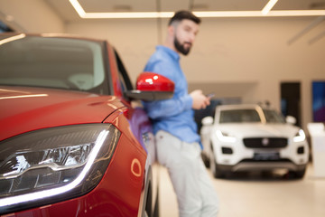 Selective focus on car lights, man using smart phone, leaning on a car on the background. Technology, buying auto concept