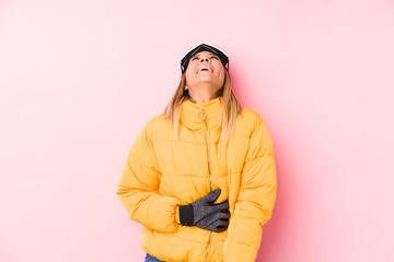 Young caucasian woman wearing a ski clothes in a pink background relaxed and happy laughing, neck stretched showing teeth.
