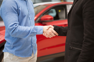 Fototapeta premium Cropped shot of a car dealer shaking hands with his male customer after closing the deal. Man buying car, shaking hands with salesman
