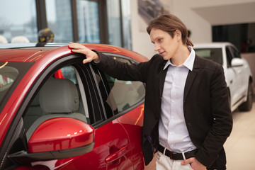 Young businessman examining modern automobile on sale at car dealership, copy space