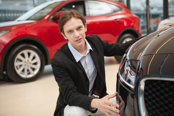 Fototapeta na wymiar Young elegant man looking to the camera confidently while examining cars on sale at the dealership