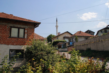 Fototapeta na wymiar cozy rural houses among the trees and the river with visible minarets of the mosque. Architecture of residential buildings in Bosnia and Herzegovina.