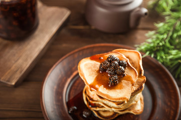 Siberian dessert - young pine cones jam. Ukrainian cone jam in a jar on a dark background close-up and copy space. Fritters with jam on a plate. Pancakes with jam.