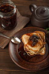 Siberian dessert - young pine cones jam. Ukrainian cone jam in a jar on a dark background close-up and copy space. Fritters with jam on a plate. Pancakes with jam.