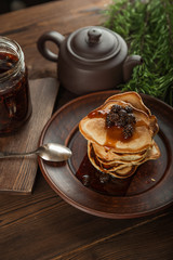 Siberian dessert - young pine cones jam. Ukrainian cone jam in a jar on a dark background close-up and copy space. Fritters with jam on a plate. Pancakes with jam.