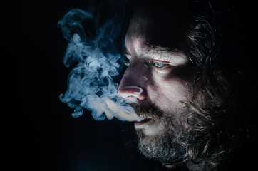 Side profile of a smoking man in low key exhaling, islolated, with copy space.