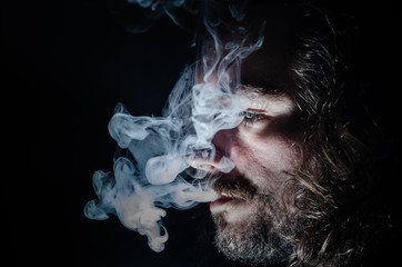 Side profile of a smoking man in low key exhaling, islolated, with copy space.