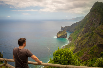 Fototapeta premium Homem a olhar para bonita paisagem de penhasco à beira mar e montanhas com vegetação