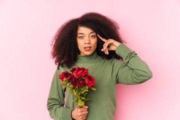 Young afro woman holding a roses isolated Young afro woman holding a rosespointing temple with finger, thinking, focused on a task.