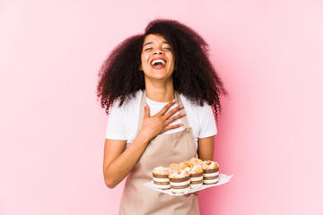 Young afro pastry maker woman holding a cupcakes isolatedYoung afro baker woman laughs out loudly keeping hand on chest.